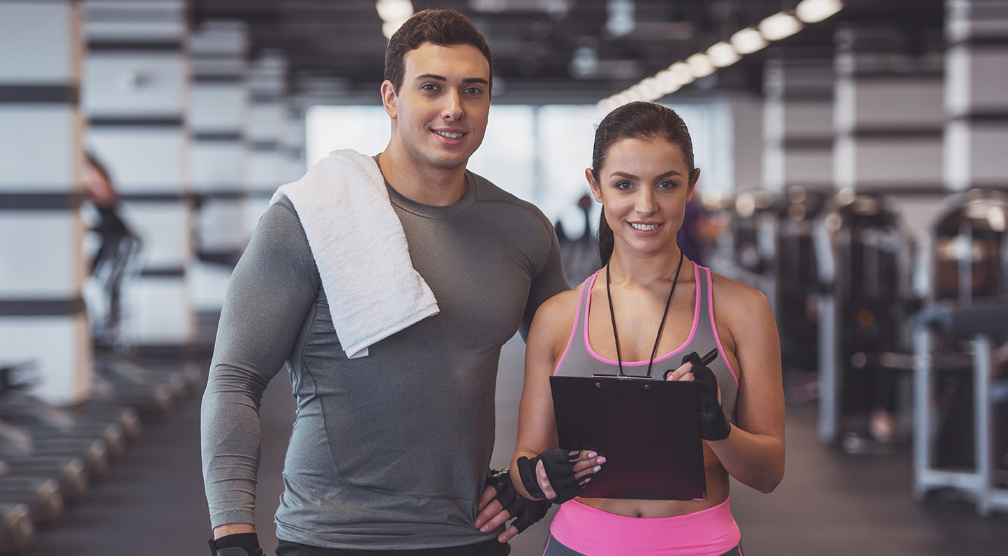 Attractive young muscular man and woman doing plank exercise while working out in gym